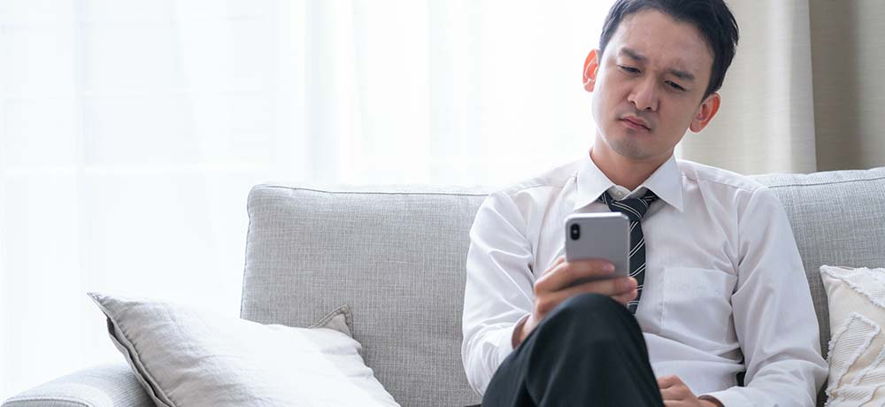 難しい顔でスマホを見る男性の写真