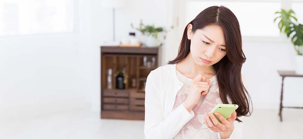 スマホを見て難しい顔をする女性の写真